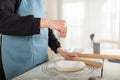 Chef in apron sprinkles flour on cooked wheat pastry dough on silicone baking mat. Selective focus, copy space