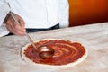 Chef baker spreading sauce on pizza base