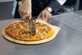 Chef baker in white uniform cutting freshly pizza slices on wooden board in kitchen. Royalty Free Stock Photo