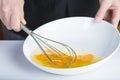 Chef beating eggs in a bowl witha a manual mixer