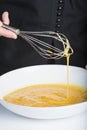 Chef beating eggs in a bowl witha a manual mixer