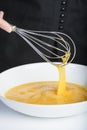 Chef beating eggs in a bowl witha a manual mixer