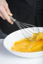 Chef beating eggs in a bowl witha a manual mixer