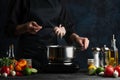 The chef in black apron cooking baby octopus on the professional kitchen. Chef`s hand putting seafood into the pot with boiling