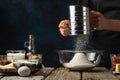The chef in black apron sifts flour into glass bowl for preparing dough. Backstage of cooking waffle on rustic wooden table with Royalty Free Stock Photo