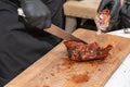 Chef in black gloves cuts juicy meat steak on the wood board with the knife, close-up. Delicious, juicy, freshly cooked meat Royalty Free Stock Photo