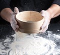 Chef in a black uniform holds in his hand a round wooden sieve