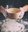 Chef in a black uniform holds in his hand a round wooden sieve