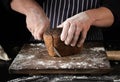 Chef in black uniform holds a kitchen knife in his hand and cuts off pieces of bread from a baked brown rye flour loaf Royalty Free Stock Photo