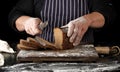 Chef in black uniform holds a kitchen knife in his hand and cuts off pieces of bread from a baked brown rye flour loaf Royalty Free Stock Photo