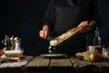 Chef in black uniform pours chopped onion from wooden board into plate on rustic table with ingredients background. Frozen motion Royalty Free Stock Photo