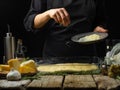 A chef in a black uniform prepares focaccia-Italian bread, pie, pizza from the ingredients that lie on a wooden table. Sprinkle Royalty Free Stock Photo