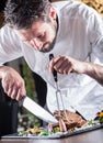 Chef. Chef with knife and fork. Professional chef in a restaurant or hotel prepares or cut up t-bone steak. Chef preparing steak. Royalty Free Stock Photo