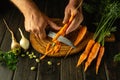 The chef cleans fresh carrots on the kitchen table before adding them to the vegetable borscht. Close-up of a cook hands with a