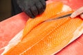 Closeup fresh salmon fish preparing fillet with knife on red cutting board in professional kitchen of restaurant. Concept Japanese Royalty Free Stock Photo