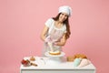 Chef cook confectioner or baker in white t-shirt toque chefs hat cooking at table isolated on pink pastel background in