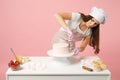Chef cook confectioner or baker in white t-shirt toque chefs hat cooking at table isolated on pink pastel background in