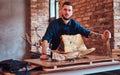 Chef cook holds knife and posing near a table with exclusive jerky meat in a kitchen with loft interior. Royalty Free Stock Photo