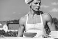 Chef cook with nude muscular torso. Man on confident face wears cooking hat and apron, skyline on background. Cook