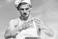 Chef cook preparing dough for baking with flour. Man on busy face wears cooking hat and apron, sky on background. Cook Royalty Free Stock Photo