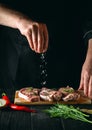 Chef or cook sprinkles the meat with salt. Preparing meat before baking. Working environment in kitchen of restaurant or cafe Royalty Free Stock Photo