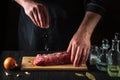 Chef or cook sprinkles the raw beef meat with salt. Preparing meat before baking. Working environment in kitchen of restaurant or Royalty Free Stock Photo