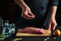 Chef or cook sprinkles raw meat with salt. Preparing beef meat before baking. Working environment in the kitchen of restaurant or Royalty Free Stock Photo