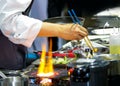 Chef cooking with flame in a frying pan on a kitchen stove, Chef in restaurant kitchen at stove with pan, doing flambe on food Royalty Free Stock Photo