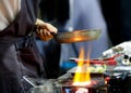 Chef cooking with flame in a frying pan on a kitchen stove, Chef in restaurant kitchen at stove with pan, doing flambe on food Royalty Free Stock Photo