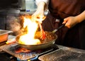 Chef cooking with flame in a frying pan on a kitchen stove, Chef in restaurant kitchen at stove with pan, doing flambe on food Royalty Free Stock Photo
