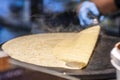 A chef cooking a large French crepe blowing smoke on a metal griddle