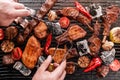 Chef cooking meat and vegetables on the grill, hand holding meat tongs on dark background. Top view, flat lay