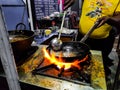 A chef cooking tadka fry in a frying pan at a road side food corner on a stove over flames