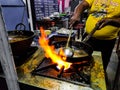 A chef cooking tadka fry in a frying pan at a road side food corner on a stove over flames