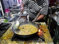 A chef cooking tadka fry in a frying pan at a road side food corner on a stove over flames