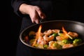 Chef cooks with fire in a pan shrimp with vegetables. On a black background, restaurant service