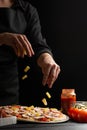 Chef cooks Italian pizza, sprinkles with pineapple. Freezing in motion. Against the background of pizza ingredients. Black Royalty Free Stock Photo