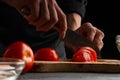 The chef cooks, slices tomatoes for cooking. on a black background. recipe book and tasty wholesome food. cooking specials