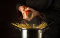 The chef cooks spaghetti in a pot with steam in the kitchen. Adding aromatic pepper. Free space for advertising on a dark