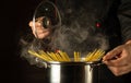 The chef cooks spaghetti in a pot with steam in the kitchen. Molecular cuisine. Free space for advertising on a dark background