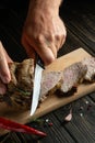 The chef cuts the baked veal meat with a knife for cooking dinner in the kitchen. Fast street food concept on dark background Royalty Free Stock Photo