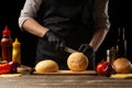 Chef cuts a fresh, crispy bun with sesame, for making a delicious burger or hamburger. Against the background with ingredients Royalty Free Stock Photo