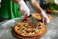 Chef cuts freshly prepared pizza on a wooden substrate.