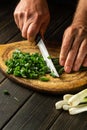 The chef cuts green onion leaves on a vintage cutting board before preparing a delicious dish or a vegetarian diet Royalty Free Stock Photo