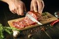 Chef cuts grilled beef meat on cutting board. Work environment on kitchen table with condiments or spices. Black background Royalty Free Stock Photo