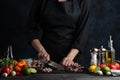 Chef cuts with knife boiled octopuses for cooking traditional asian dish. Backstage of preparing seafood on dark blue background. Royalty Free Stock Photo