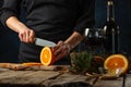 Chef cuts with knife juicy orange on wooden chopped board for preparing mulled wine on rustic wooden table with festive