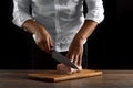 The chef cuts a piece of fresh meat on a wooden board against a dark background, hands close-up. The concept of cooking, cooking Royalty Free Stock Photo