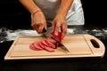 Chef cuts salami sausage for making homemade italian pizza on a wooden cutting board Royalty Free Stock Photo