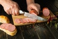 The chef cuts veal sausage on a wooden cutting board. The concept of making delicious sandwiches for a snack Royalty Free Stock Photo